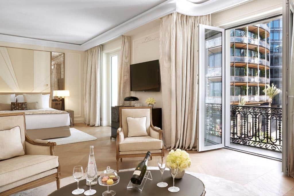 Quarto do Hôtel de Paris Monte-Carlo. Uma mesa redonda na frente com champagne, ao redor duas poltronas. Atrás uma televisão no lado direito e no meio a cama de casal. No lado direito do quarto duas portas para a sacada do quarto. Foto para ilustrar post sobre Hotéis em Mônaco.