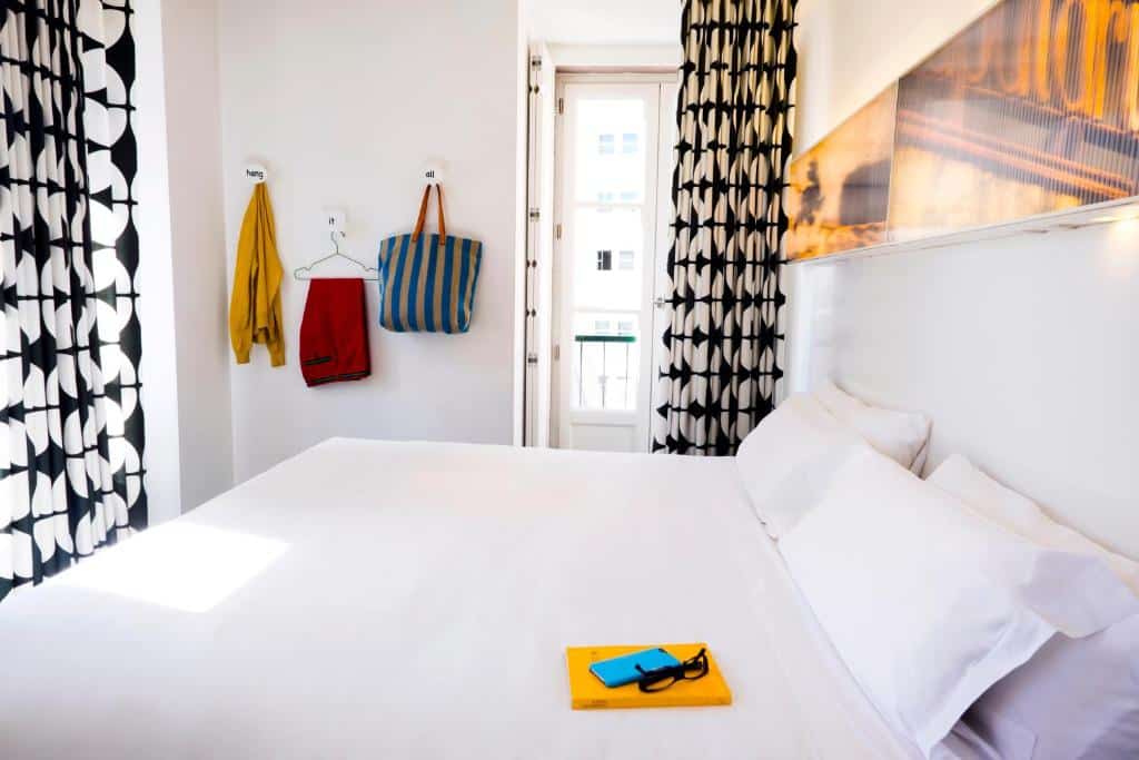 Quarto do Hotel Gat Rossio com uma cama de casal, uma pequena sacada, um pequeno quadro na parede atrás da cama, para representar hotéis baratos em Lisboa