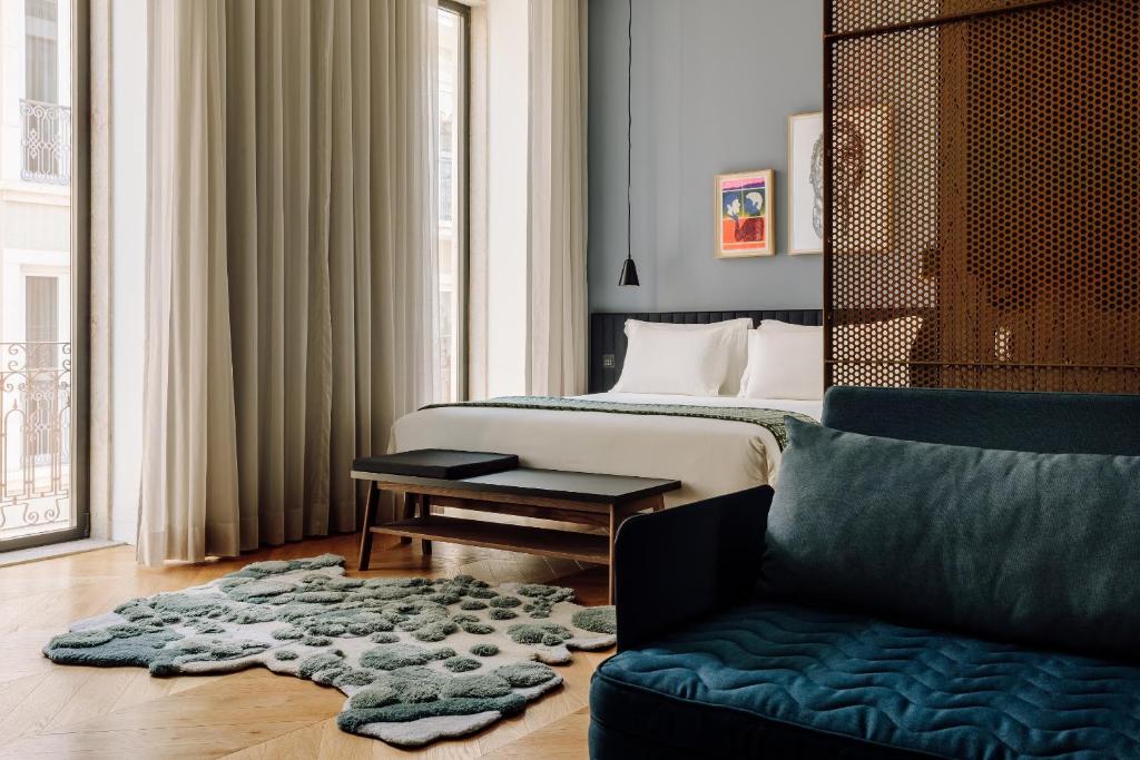 Quarto do Hotel Hotel - Member of Design Hotels com uma ampla cama de casal, duas janelas que vão do teto ao chão com cortinas, um pequeno sofá azul e um tapete