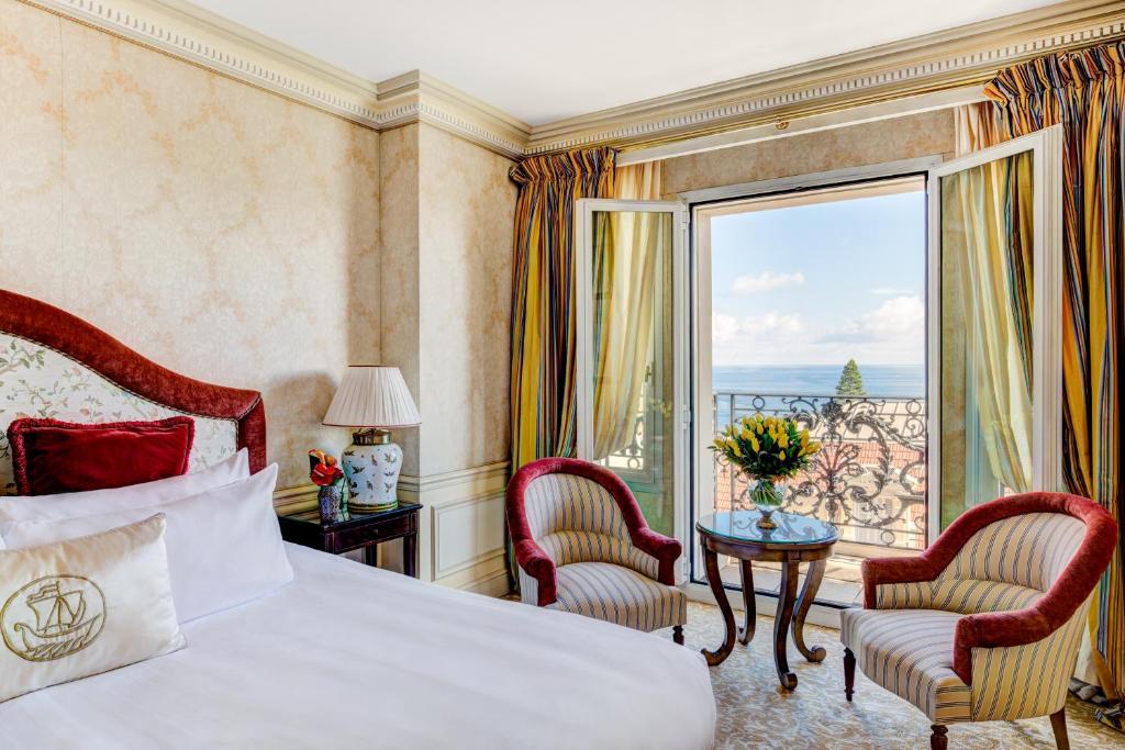 Quarto do Hôtel Métropole Monte-Carlo - The Leading Hotels of the World. Uma cama de casal no lado esquerdo, do lado da cama uma mesinha redonda com duas cadeiras. Atrás a sacada com vista para o mar. Foto para ilustrar post sobre Hotéis em Mônaco.