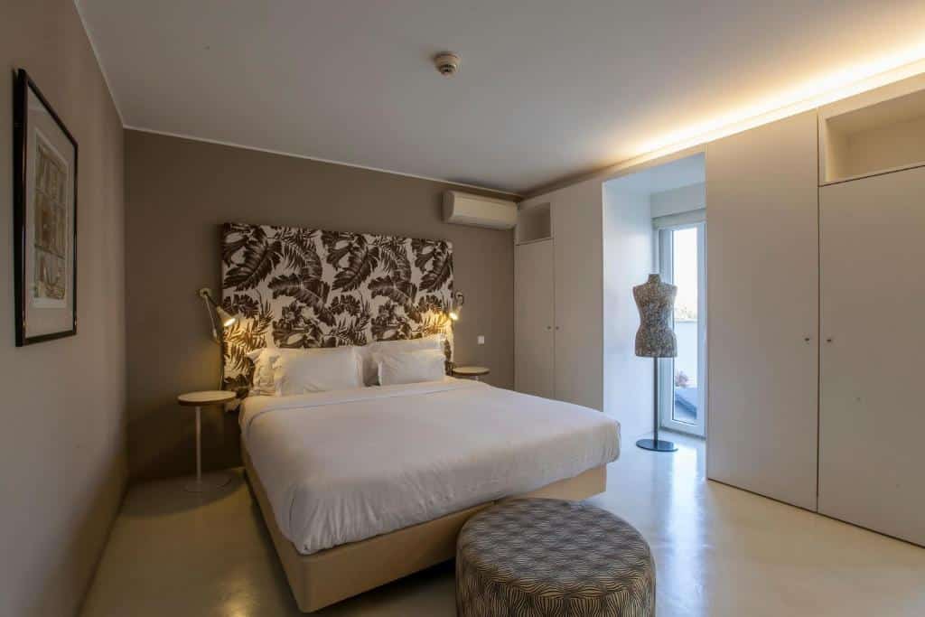 Quarto espaçoso do Hotel Pateo - Lisbon Lounge Suites, do lado direito há uma armário com duas portas, uma porta que leva para um pequeno terraço e mais um pequeno armário embutido, no centro do ambiente há uma cama de casal com um bufe almofadado ao pé da cama