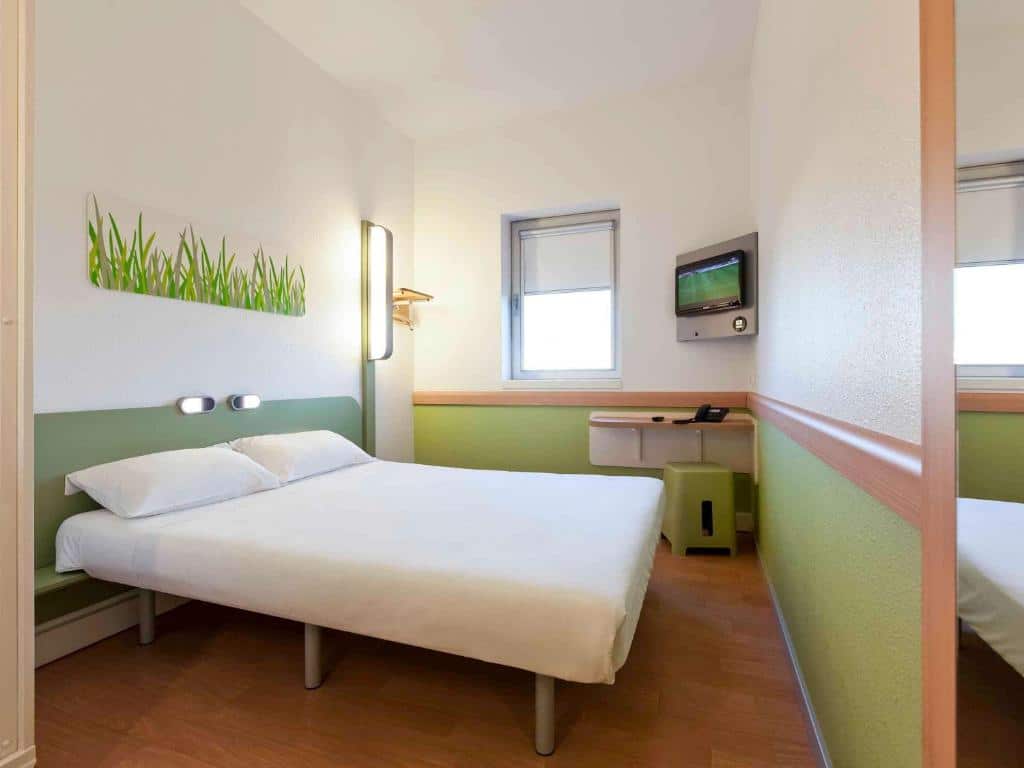 Quarto do Hotel ibis Budget Porto Gaia com cama de casal do lado esquerdo da imagem, do lado esquerdo da cama uma mesa trabalho e uma TV. Representa hotéis ibis no Porto.