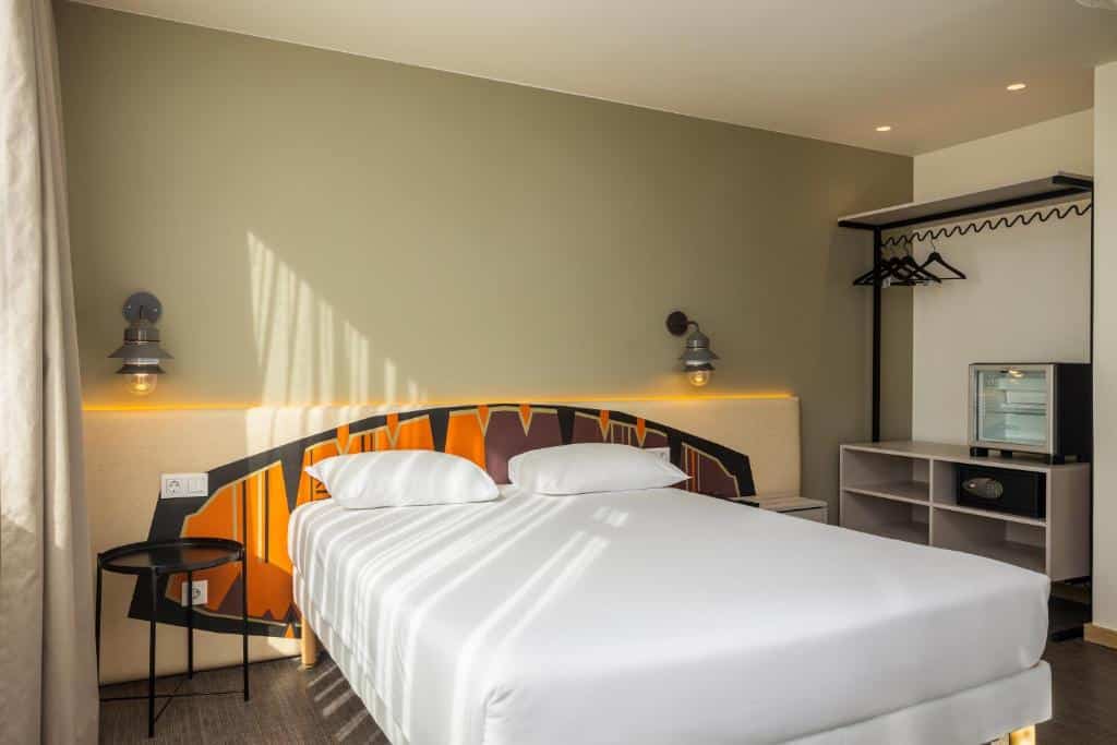 Quarto do Hotel Ibis Styles Lisboa Liberdade com uma cama de casal, um pequeno frigobar junto de um armário de conceito aberto com cabideiro