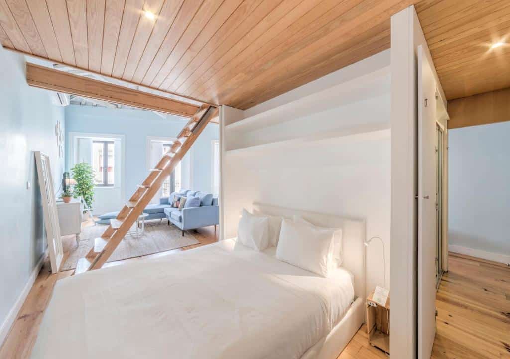 Quarto do Look At Me – Serviced Lofts & Studios com cama de casal do lado direito da iamgem, do lado esquerdo da cama uma escada de madeira que dá acesso ao andar superior, ao fundo da escada sala de estar. Representa airbnb no Porto.