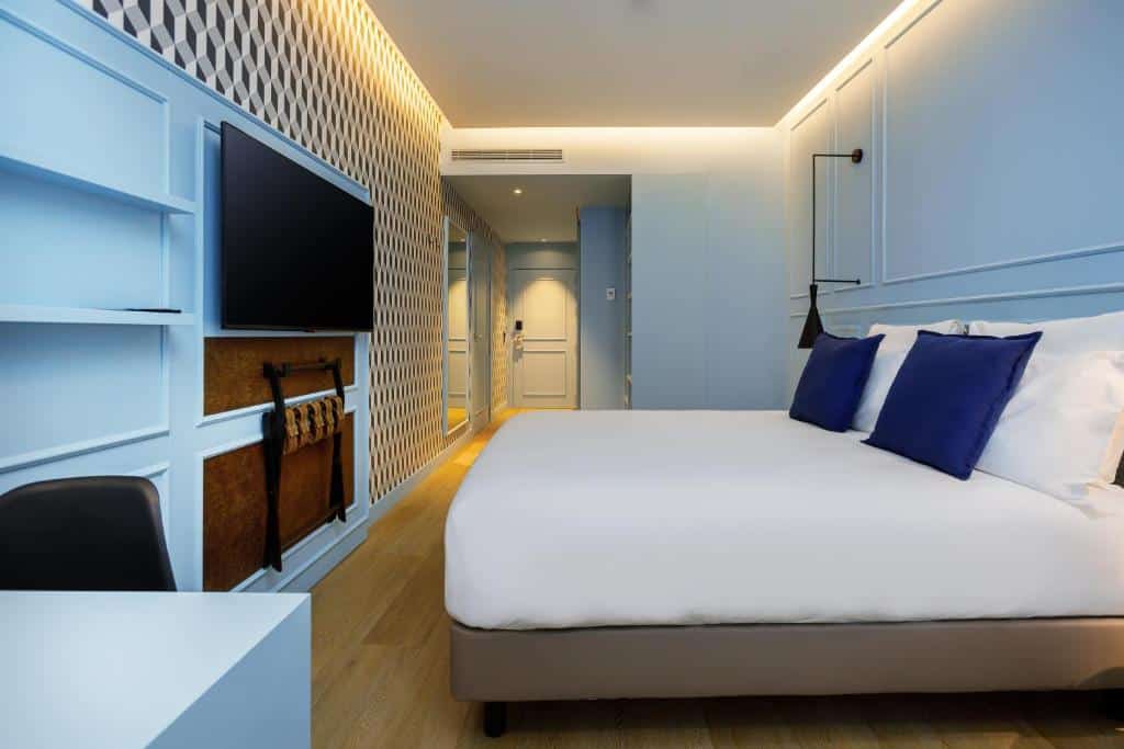 Quarto do Mercure Porto Centro Aliados com cama de casal do lado direito e em frente a cama uma TV presa na parede. Representa hotéis ibis no Porto.
