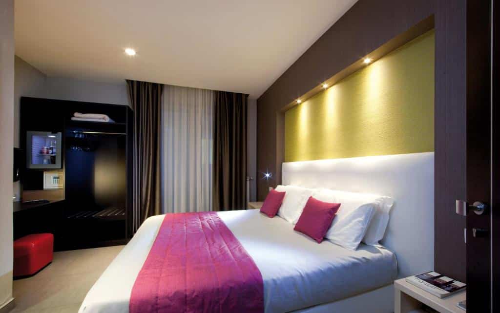 Quarto do Napolit'amo Hotel Medina com uma cama de casal, ao lado uma mesinha com objetos e ao fundo um guarda-roupa aberto para guardar objetos.