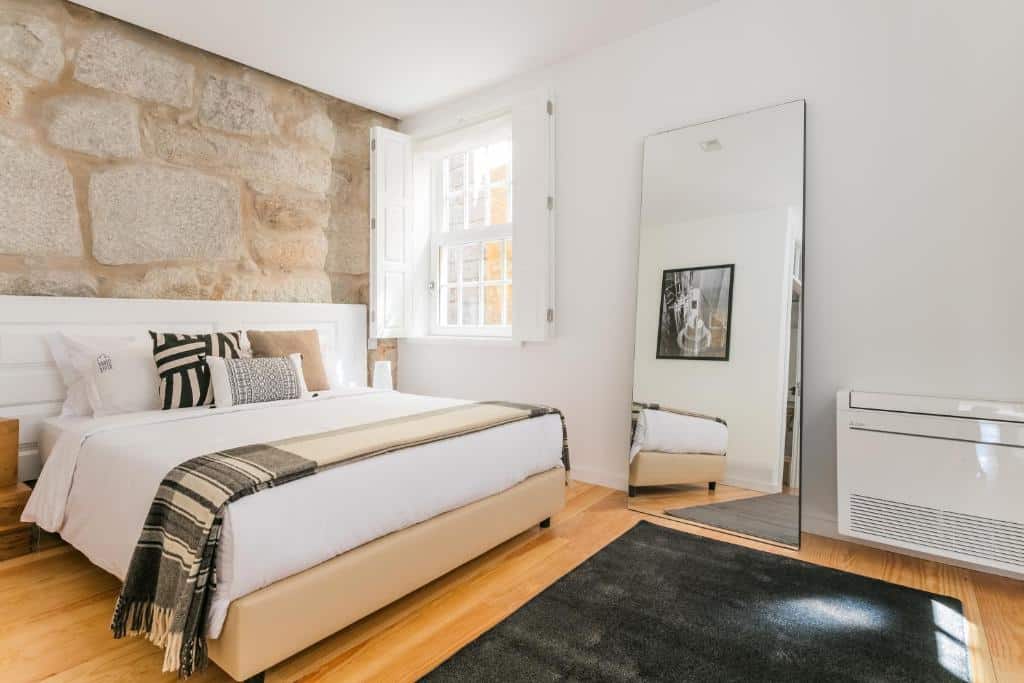 Quarto do Porto River com cama de casal do lado esquerdo da imagem com um espelho do lado direito. Representa airbnb no Porto.