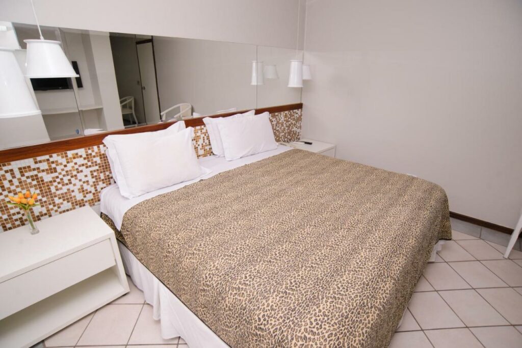 Quarto do Porty Brasil Hotel. Uma cama de casal no lado esquerdo, uma cômoda de cada lado da cama, atrás da cama um espelho.