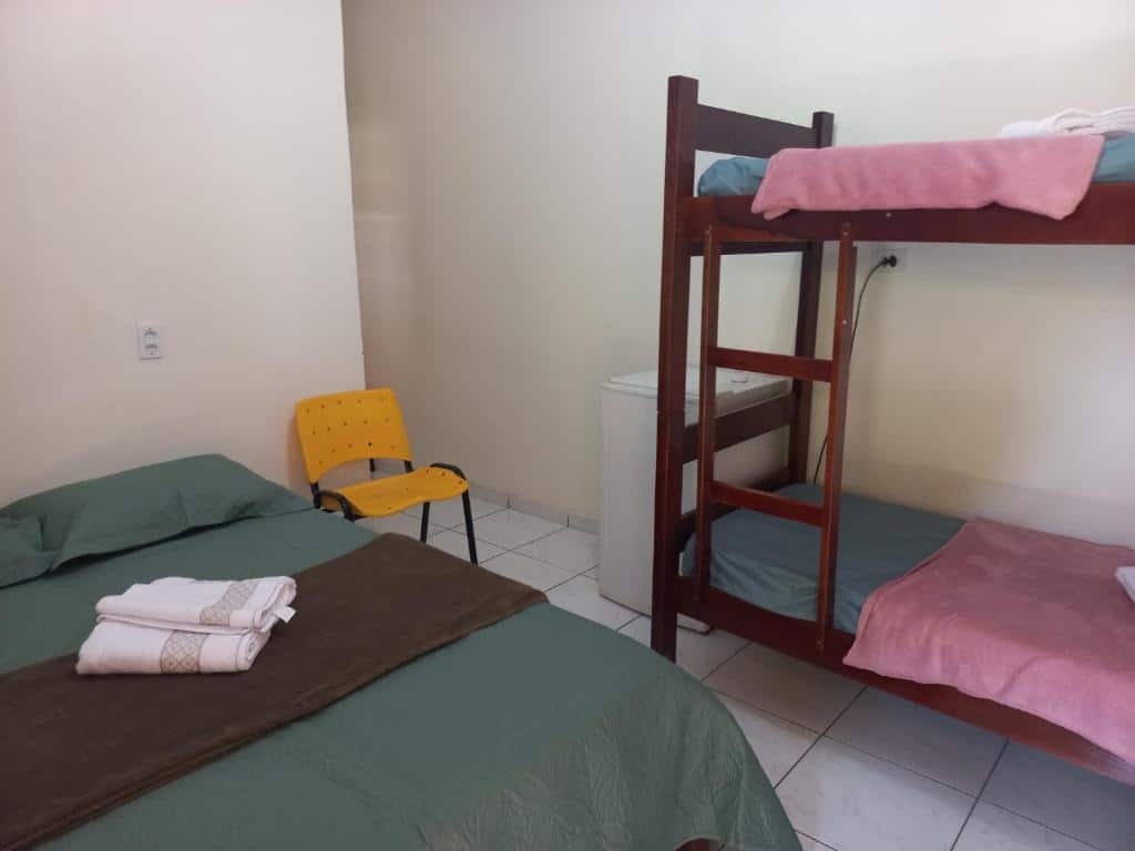 Quarto da Pousada Anayh, Nobres-MT, Vila Bom Jardim. Uma cama de casal no lado esquerdo com uma cadeira. No lado direito uma cama beliche e um frigobar e o corredor do quarto.