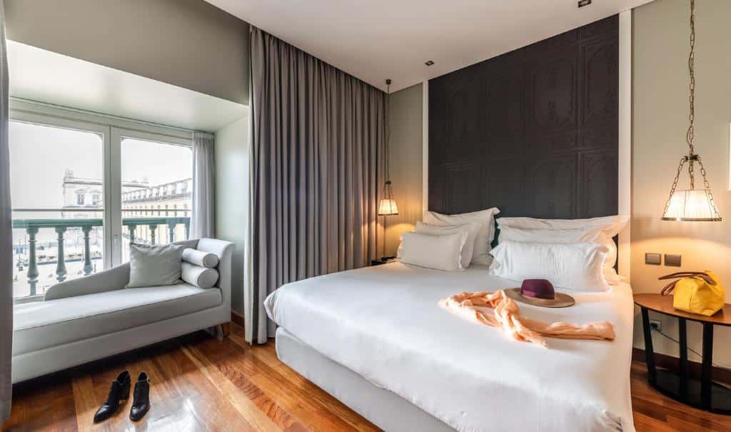 Quarto do Pousada de Lisboa - Small Luxury Hotels Of The World com uma cama de casal, há uma janela que se proteja para fora e há um pequeno sofá ali, o chão imita madeira e há duas mesinhas de cabeceira