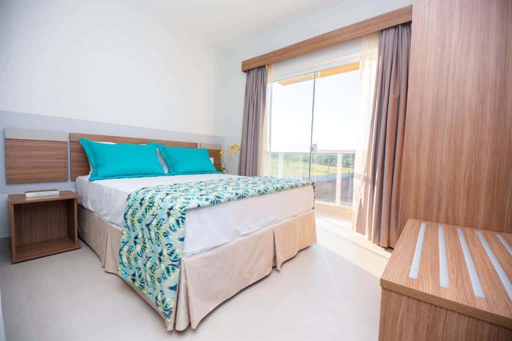 Quarto do Prive Ilhas do Lago – Oficial com cama de casal do lado esquerdo da imagem, com uma cômoda do lado esquerdo da cama.  Representa resorts em Caldas Novas.