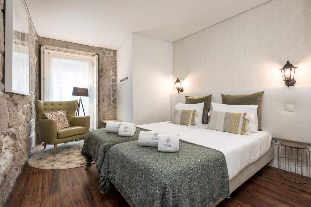 Quarto do Rua de Trás Apartments com uma cama de casal do lado direito da imagem do lado esquerdo da cama uma poltrona verde claro. Representa onde ficar no Porto.