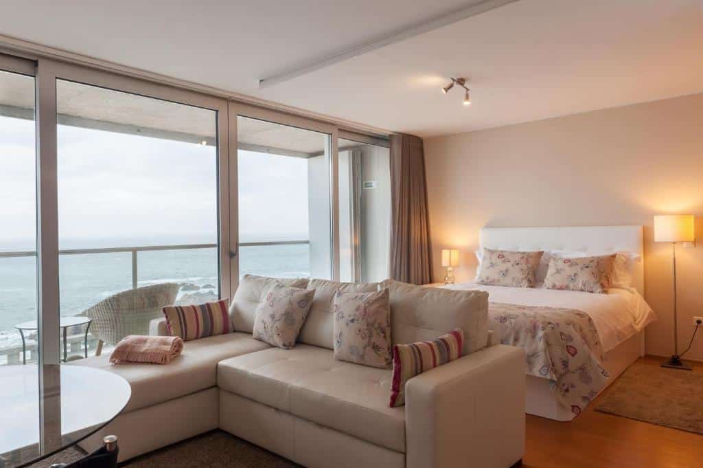 Quarto do Bartolomeu Beach Apartments com cama de casal do lado direito da imagem, no pé da cama um sofá. Representa airbnb no Porto.