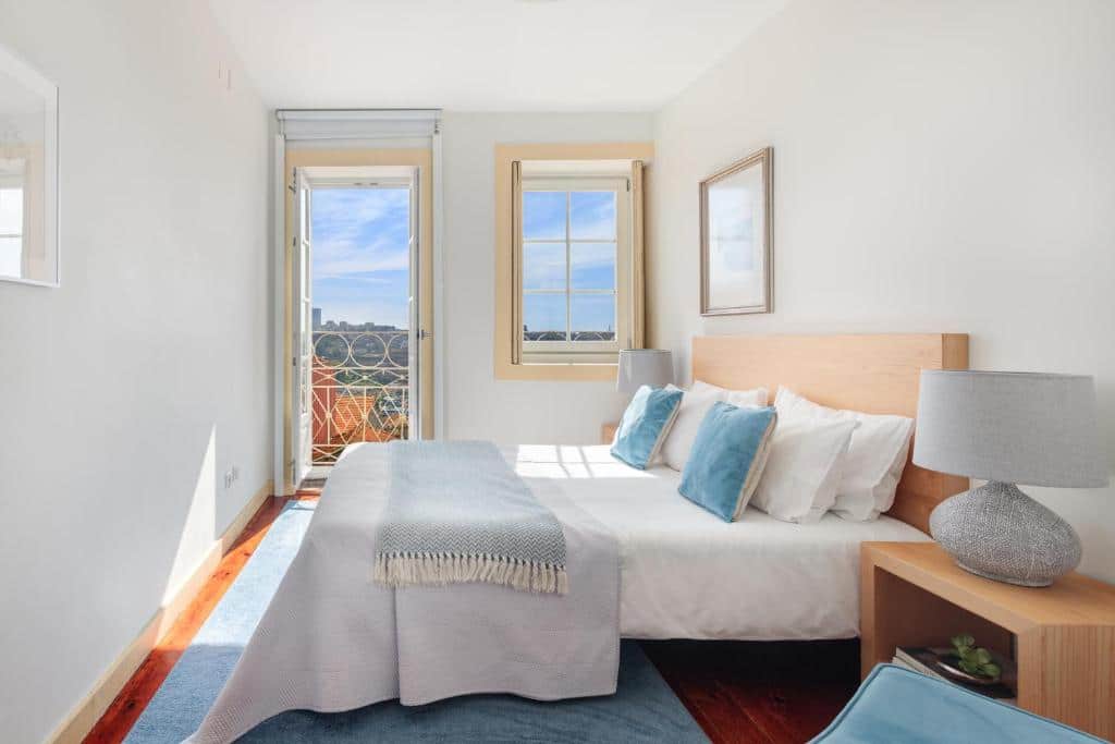 Quarto do São Miguel Apartments com cama de casal do lado direito da imagem e em cada lado da cama duas cômodas com luminária.