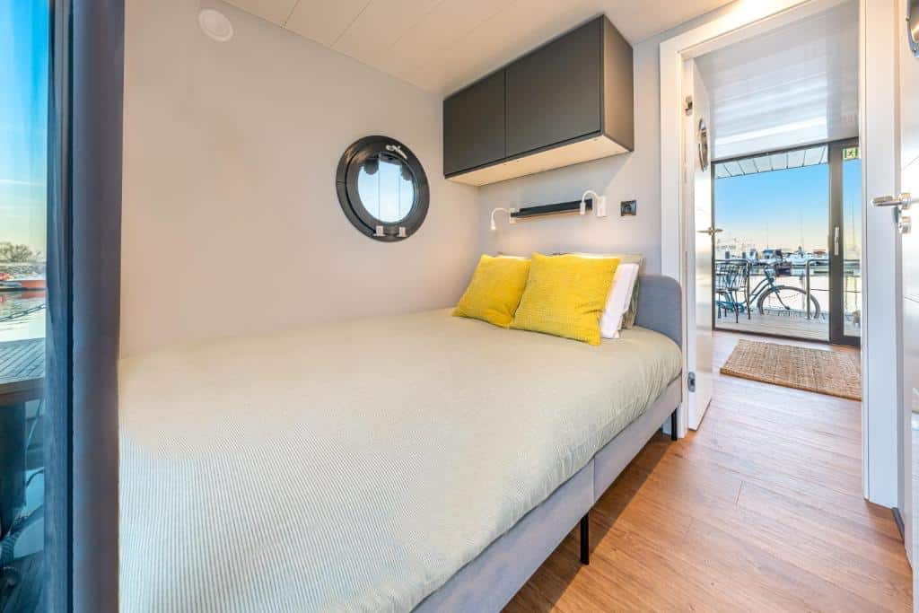 Quarto do The Homeboat Company Parque das Nações-Lisboa com uma pequena cama de casal, uma janela redonda e um móvel com duas portas sob a cama