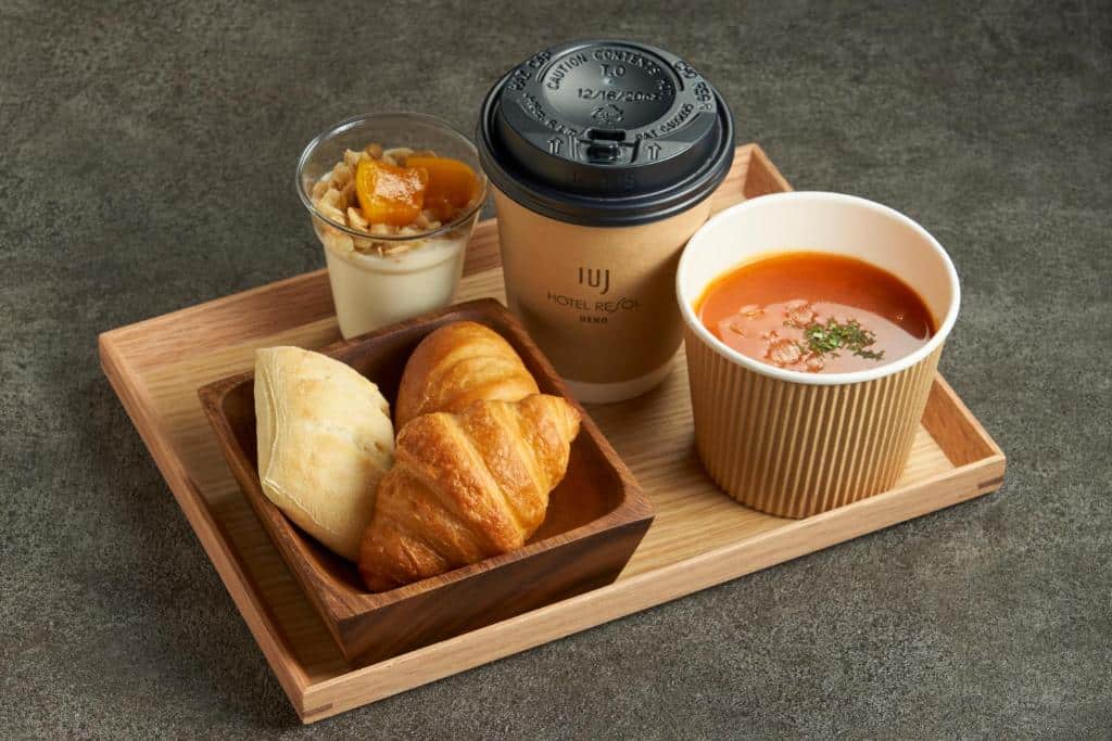 Foto de uma bandeja de madeira do Hotel Resol Ueno, servindo uma massa, um croissant, um iogurte, uma sopa e um café.