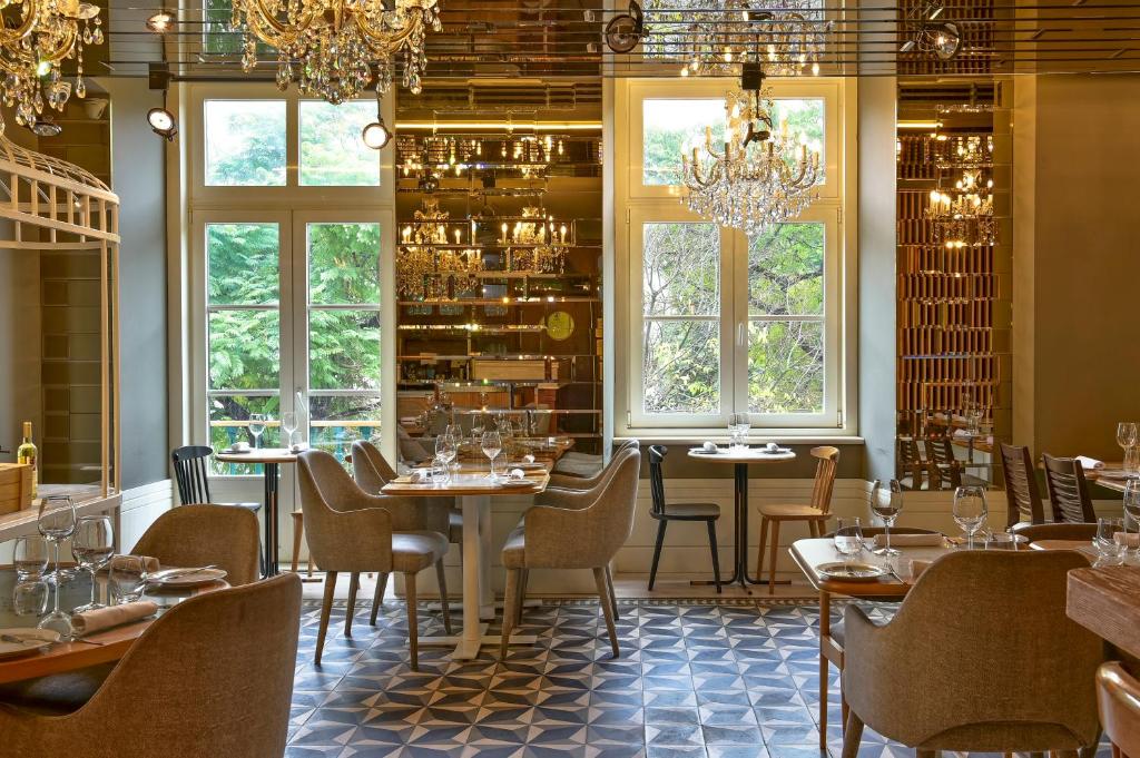 Área de refeições do My Story Hotel Rossio com lustres pendurados, mesas de madeira com cadeiras estofadas, e há duas janelas grandes iluminando o local