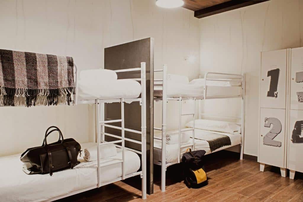 Quarto do room007 Chueca Hostel, uma das recomendações de hostels em Madri. As camas em beliche tem travesseiros e edredons, e um armário numerado está no canto do quarto. Há bolsas e um cobertor nas camas.