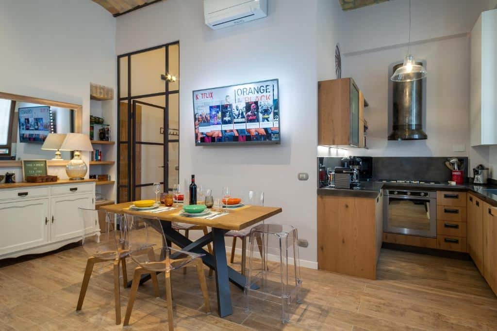 sala do One & Only Buonarroti Suite com cozinha completa conjugada, há mesa com cadeiras, tv, ar-condicionado e móveis de madeira