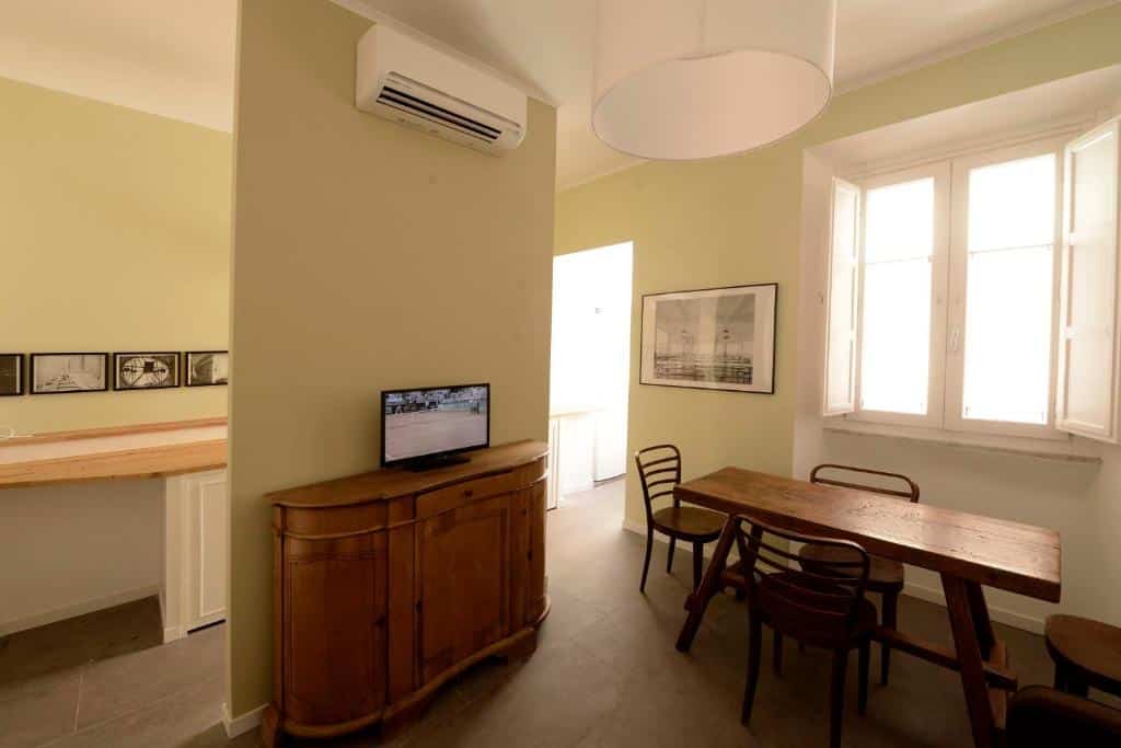 sala do Via Montebello, com móveis de madeira, aparador com tv em cima, ar-condicionado, mesa com cadeiras e janelas em um ambiente bastante arejado