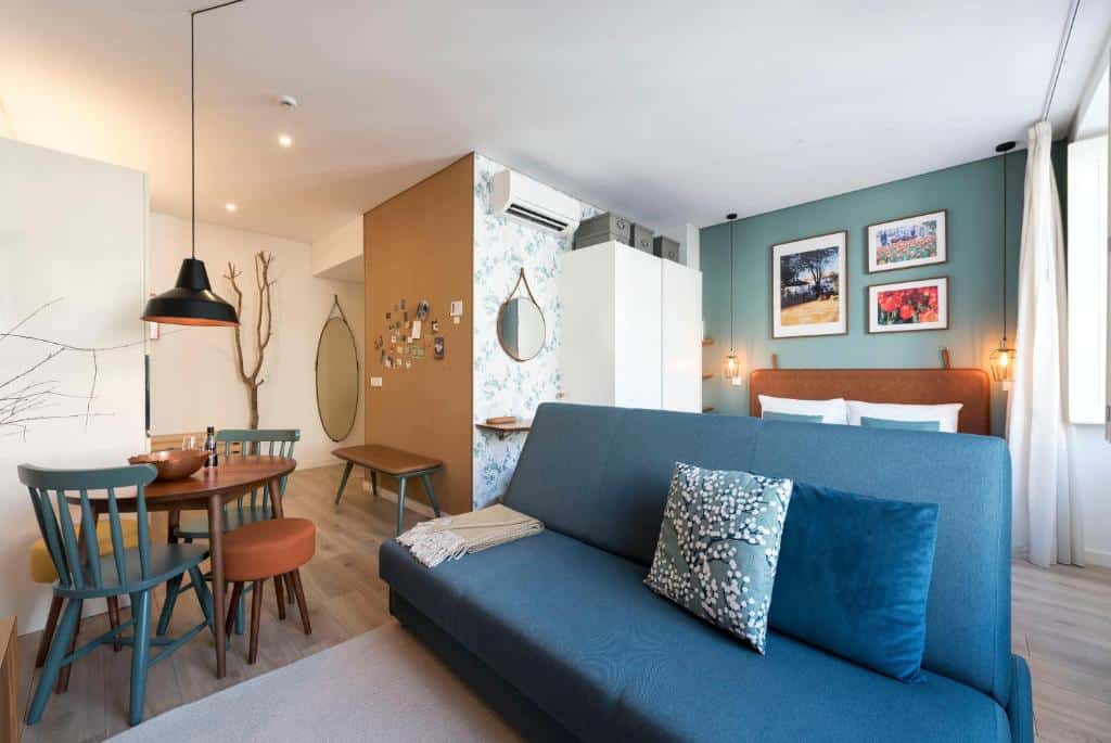 Sala de estar do Bloom House by Sweet Porto com sofá azul escuro a frente, do lado esquerdo do sofá uma mesa redonda com duas cadeiras.