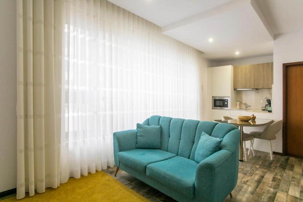 Sala de estar do Casa de Cristal com sofá azul claro a frente, ao fundo uma mesa com cadeiras e armários de cozinha.