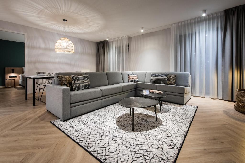 Sofá cinza em uma sala ampla com um tapete ao meio e mesinha de centro. Atrás do sofá tem uma mesa