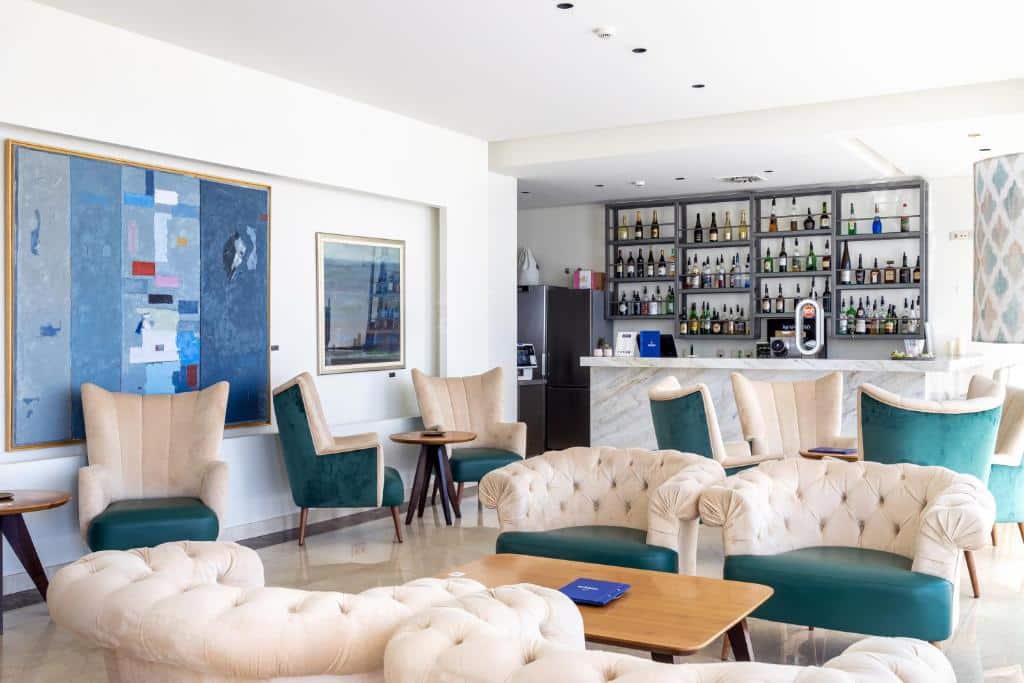 Sala de estar do Oporto Airport & Business Hotel com várias poltronas e mesas no ambiente e ao fundo um balcão e o bar.
