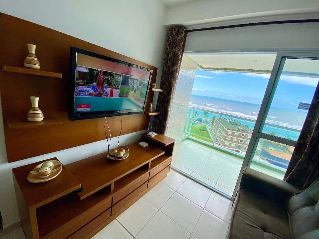 Sala de apartamento no Edifício Baalbek com móvel de madeira com televisão no lado esquerdo, sofá no lado direito e varanda com vista para o mar ao fundo.