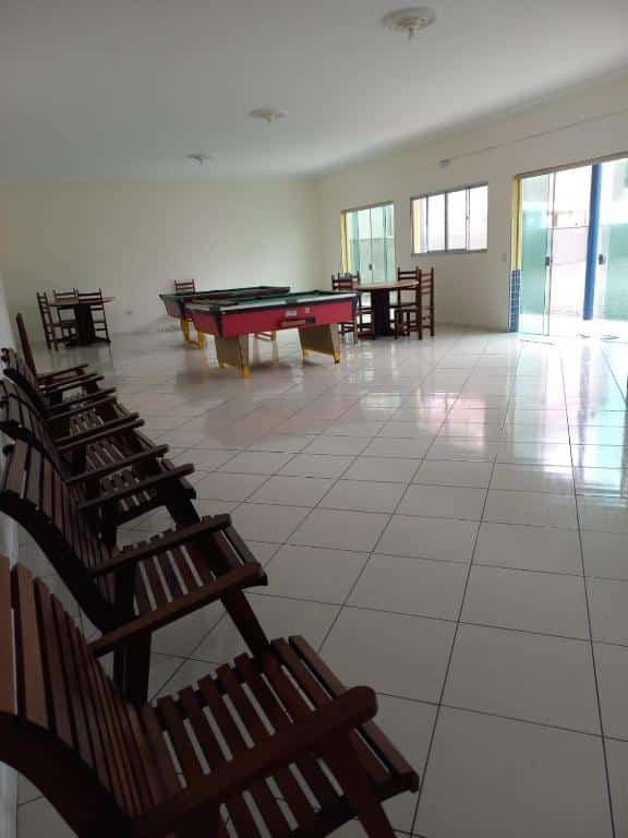 Salão de jogos com duas mesas de bilhar, mesas e cadeiras de madeira e chão de azulejo branco.