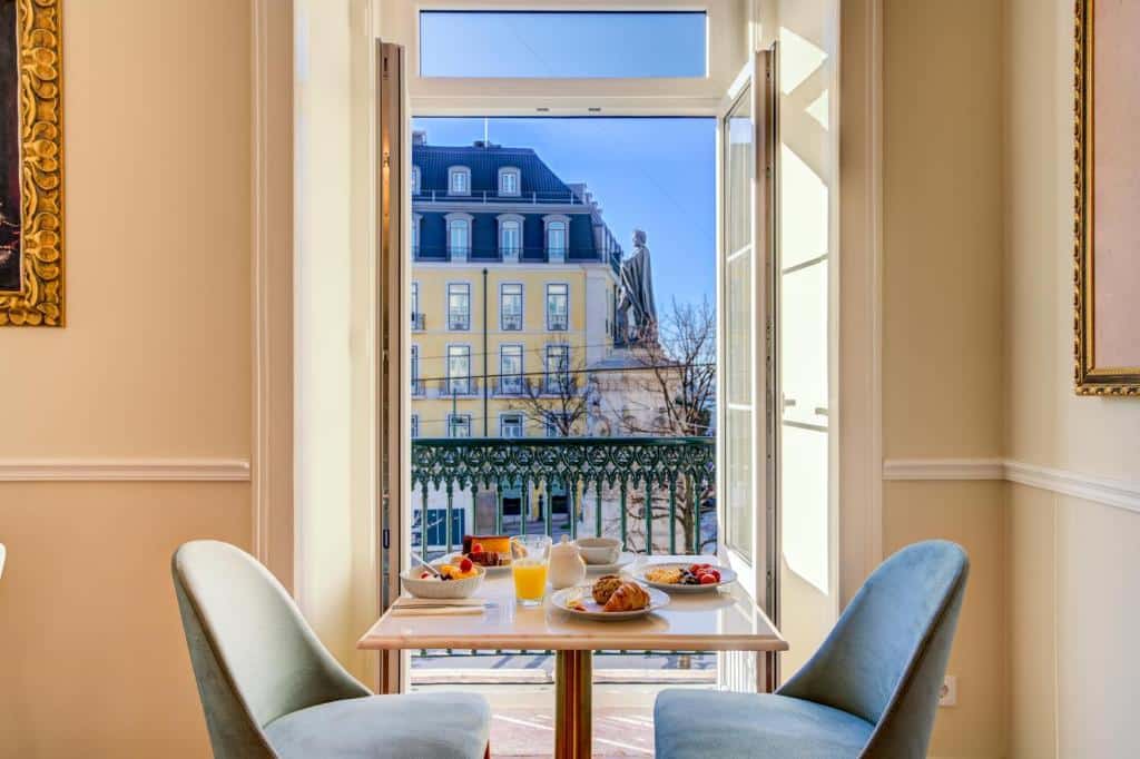 Uma pequena mesa com um café da manhã servido sob ela, junto de duas cadeiras estofadas, dentro de um dos quartos do Solar dos Poetas de frente para a varanda, para representar hotéis românticos em Lisboa