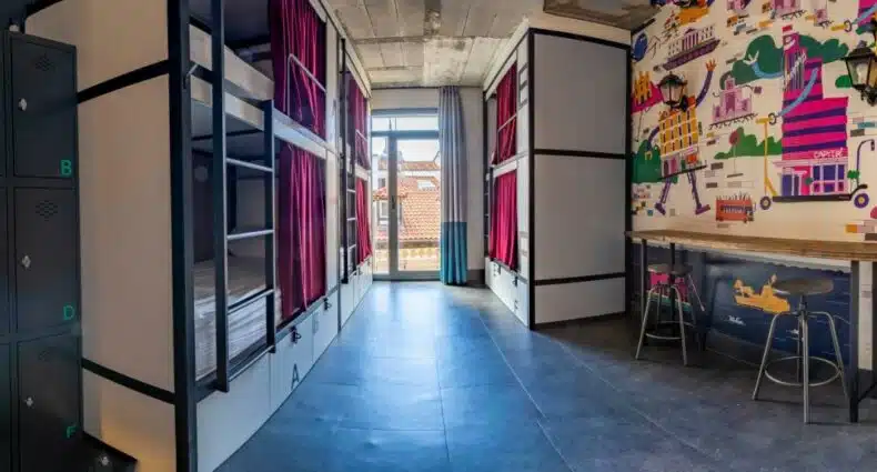 Um dormitório moderno no The Central House Madrid Lavapiés com beliches, armários, uma parede mural, janelas altas e um teto alto, para representar hostels em Madri.