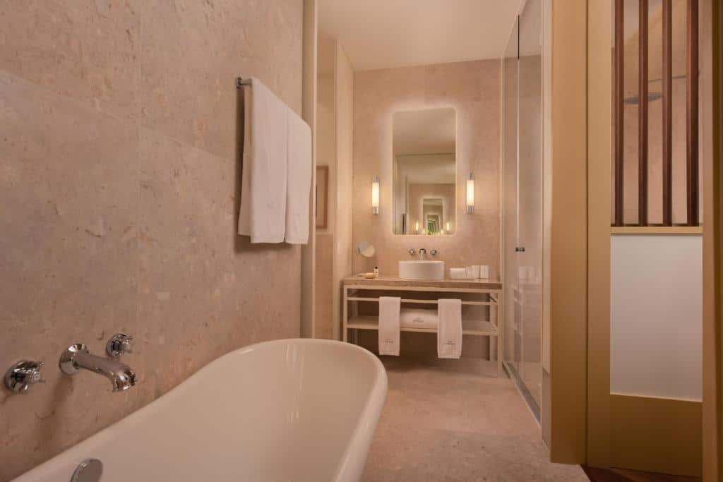 Banheiro do The Ivens Autograph Collection com uma banheira oval, um espelho, uma pia com uma cuba redonda e algumas toalhas brancas