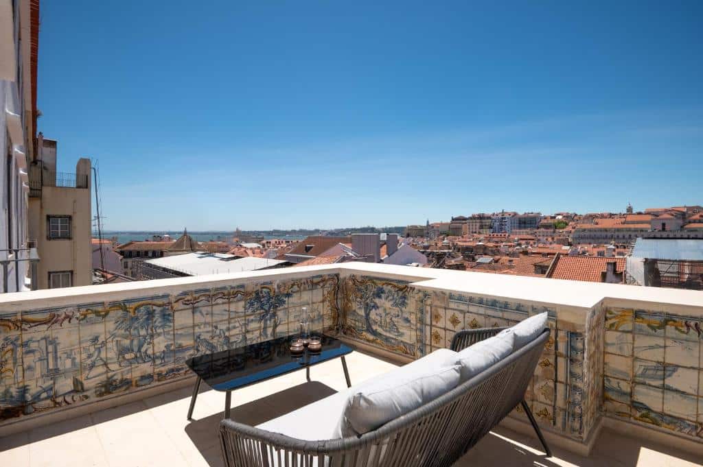 Terraço do Memoria Lisboa FLH Hotels com vista direta para os prédios históricos e, mais ao fundo, o Rio Tejo, no terraço há uma sofá com almofadas e uma pequena mesa