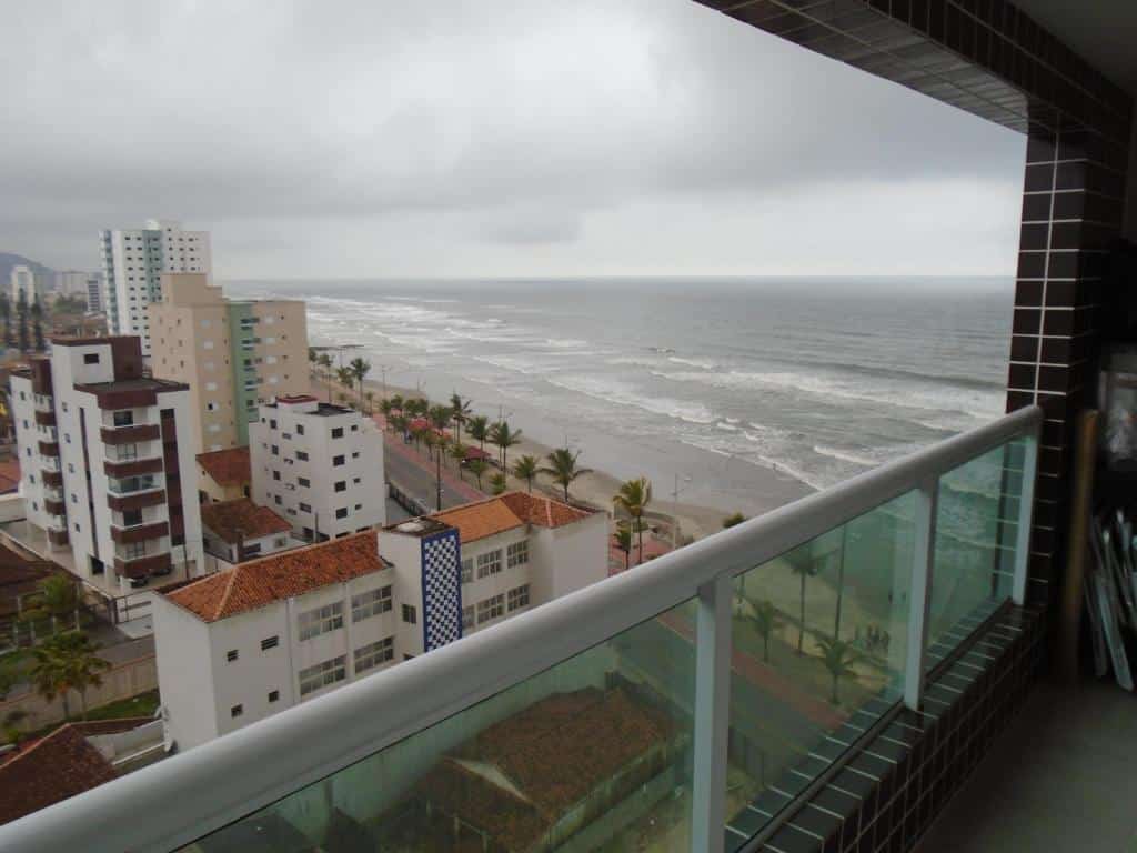 Vista da varanda de um apartamento com vista para outros prédios e para a praia.