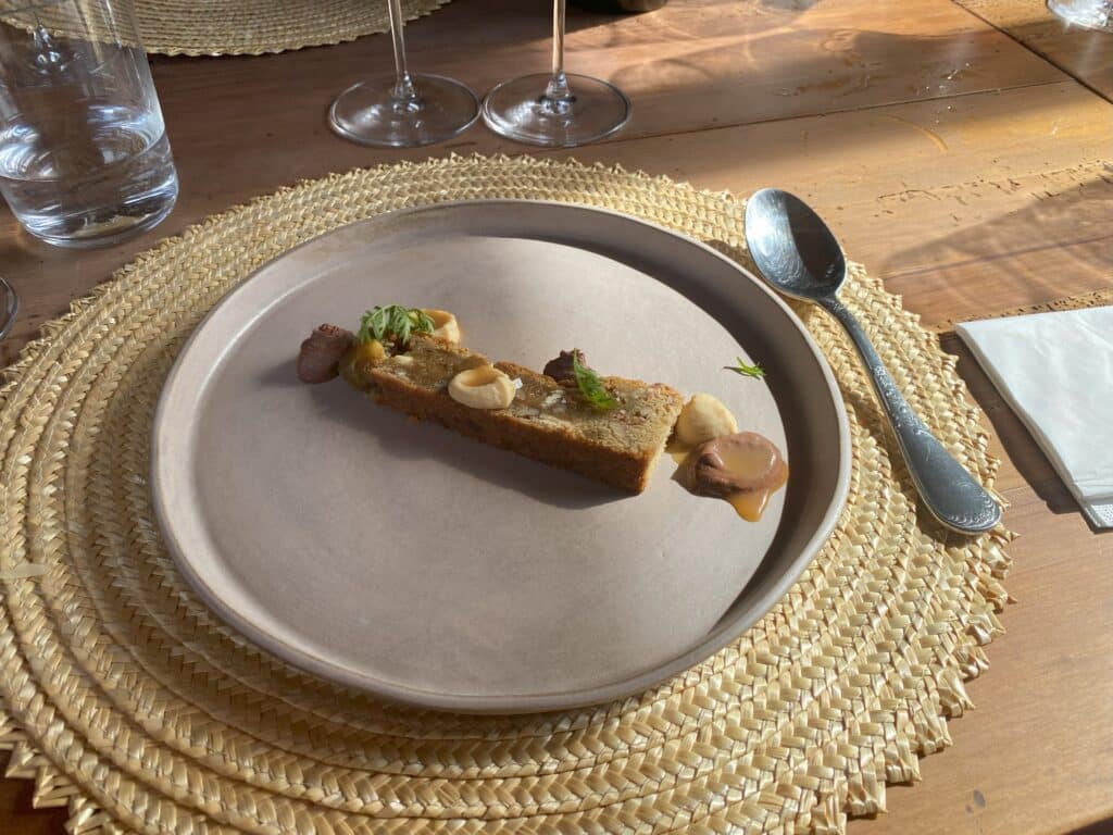 Prato de cerâmica com a única sobremesa do restaurante Apino: o torrão de chocolate branco, nuts e caramelo salgado. Há uma colher apoiada ao lado direito