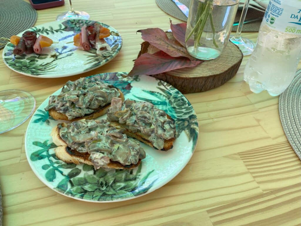 Pratos com entradas no almoço do Wine Garden, uma das dicas de restaurantes em Bento Gonçalves, sendo o que está à frente com bruschettas funghi, e ao fundo palitos com charcutaria e damasco