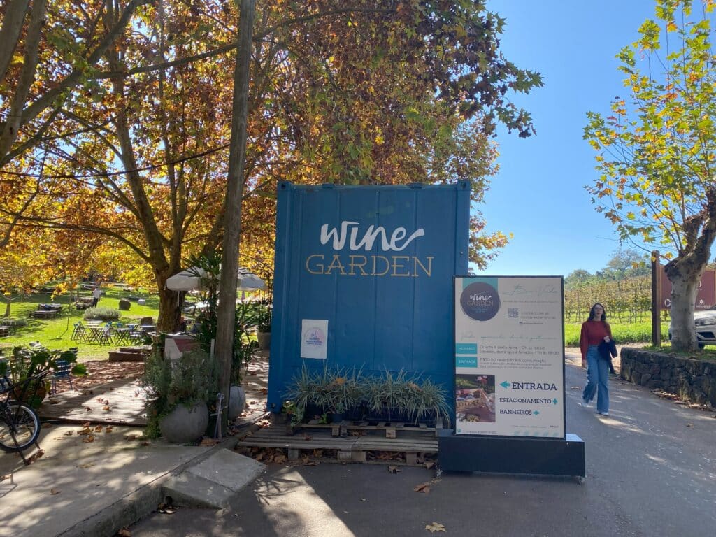 Área de entrada do Wine Garden Miolo, espaço gastronômico localizado dentro da vinícola homônima, com árvores de tons outonais ao fundo, e um céu azul sem nuvens