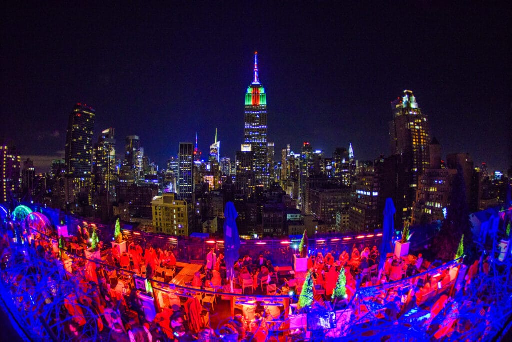 vista de uma festa de ano novo no 230 Fifth Avenue, uma das opções de o que fazer em NOva York no Réveillon, com pessoas comemorando, luzes coloridas e vista da cidade brilhante
