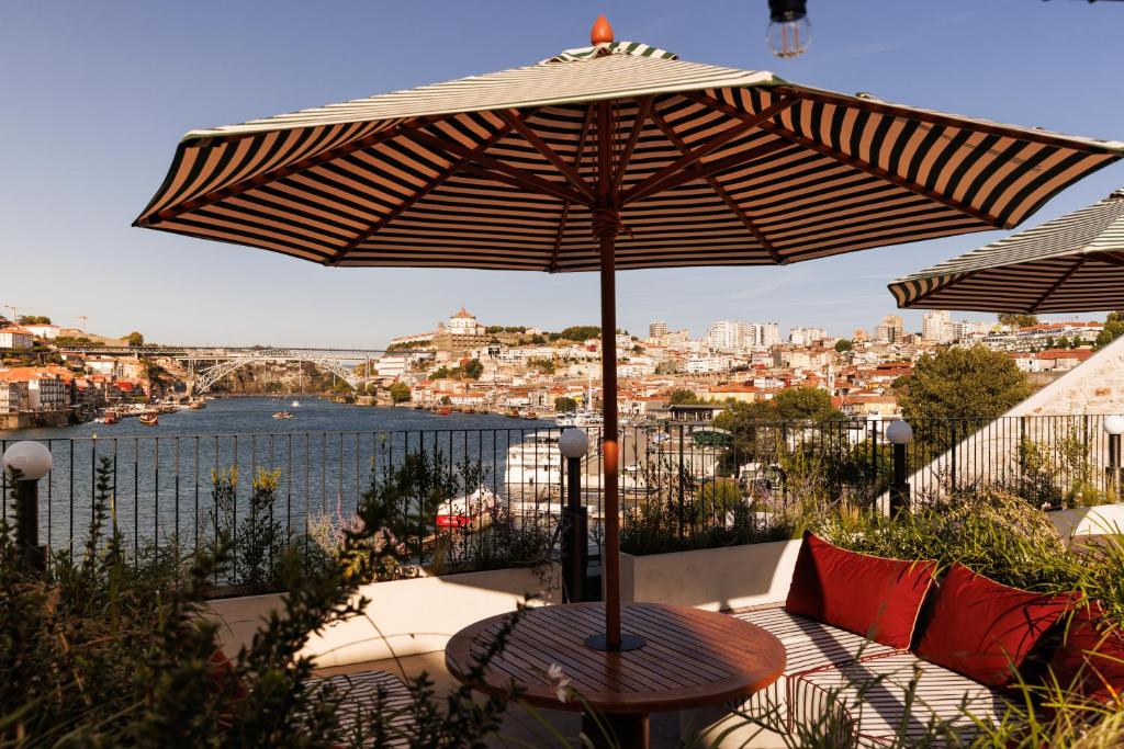 Sacada do The Rebello Hotel & Spa – Small Luxury Hotels Of The World durante o dia com banco em volta e um guarda-sol no meio em volta de muitas plantas com vista para o rio Douro.