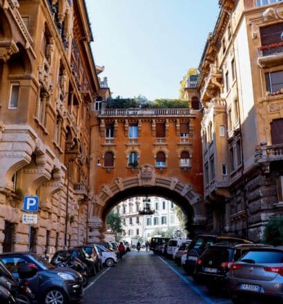diversos carros estacionados lado a lado no Bairro Coppedé, em Roma, com um belo arco e prédios históricos ricamente trabalhados, para ilustrar o post de aluguel de carros em Roma
