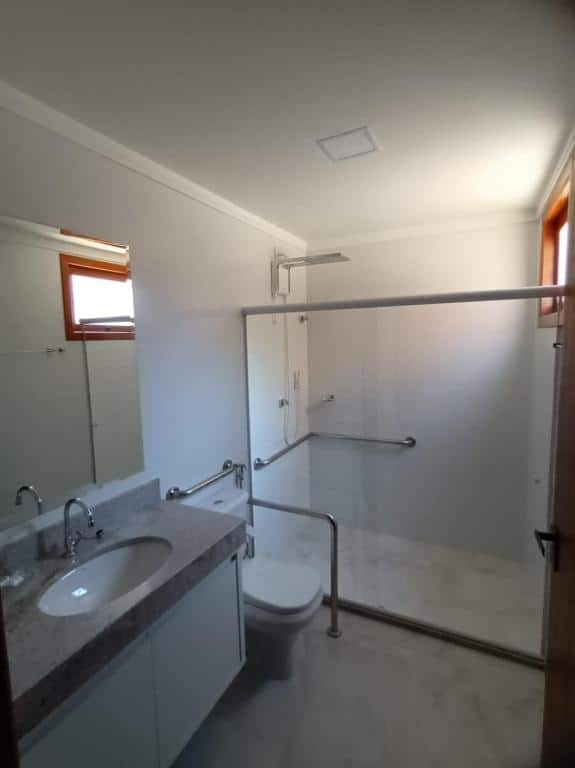 Um banheiro amplo e acessível na Pousada La Sofia. No canto inferior esquerdo vemos uma pia e espelho, ao seu lado há um vaso sanitário com barras de apoio ao seu redor. E o box do banheiro também é espaçoso e conta com outras barras de apoio.