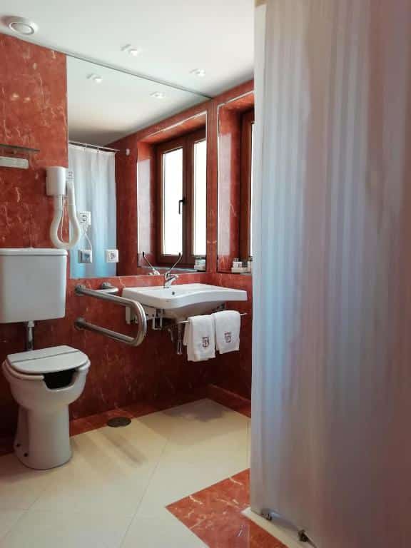 Banheiro com acessibilidade do Hotel Rural Quinta Do Pego com vaso sanitário do lado esquerdo com barra de apoio e do lado direito pia baixa com barra de apoio. Representa hotéis no Vale do Douro.