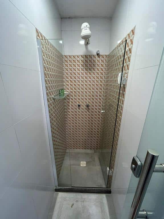 Foto do box do Bahia Pelô Hostel. O espaço possui azulejos, uma ducha e uma prateleira de vidro dentro dele para apoio de itens de banho.
