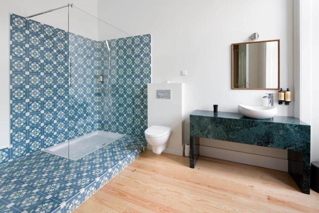 Banheiro amplo do Walewska  com um box grande de vidro com azulejos azuis, um vaso sanitário e uma pia azul com uma cuba branca, além de um espelho e itens de higiene, para representar hotéis para brasileiros em Lisboa