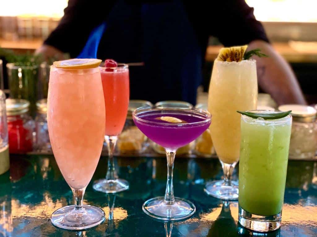 cinco drinques coloridos no bar do Pod Times Square, atrás do balcão é possível ver um homem branco com os braços apoiados na mesa. Este é um dos hotéis em Nova York.