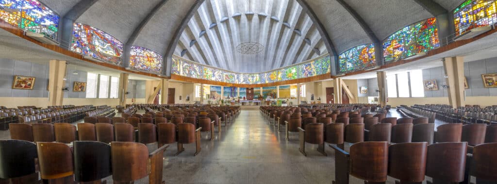 interior da catedral São Francisco Xavier de Joinville com diversas cadeiras de madeira dispostas lado a lado, formando várias fileiras até o púlpito da igreja. No teto é possível ver vários vitrais coloridos