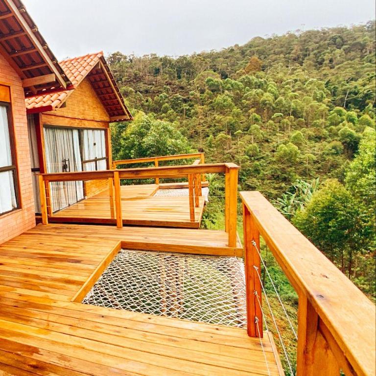 Varandas das suítes do Chalé Milão Caravaggio, que são feitas com madeira e possuem cerca de proteção. A vista é para uma vegetação com inúmeras árvores.