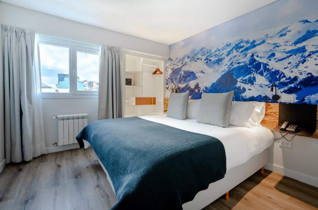 Quarto do Cilene del Fuego Suites & Spa. Uma cama de casal do lado direito, no lado direito da cama uma prateleira, do lado esquerdo um guarda-roupa e a janela do quarto. Foto para ilustrar post sobre hotéis em Ushuaia.