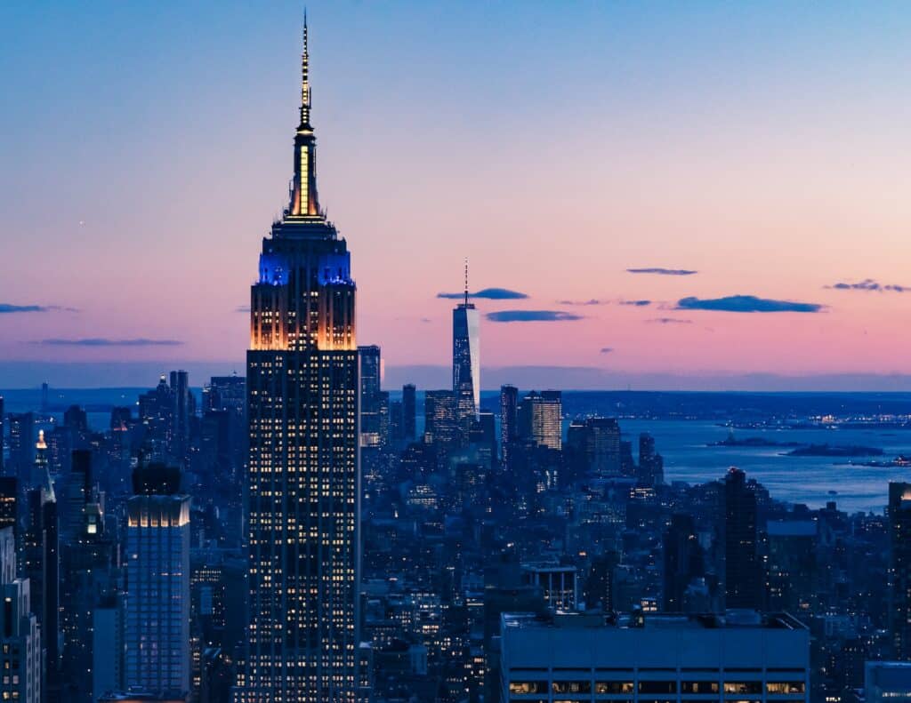 O prédio mais alto de Nova York, o Empire States iluminado de noite cercado por outros prédios